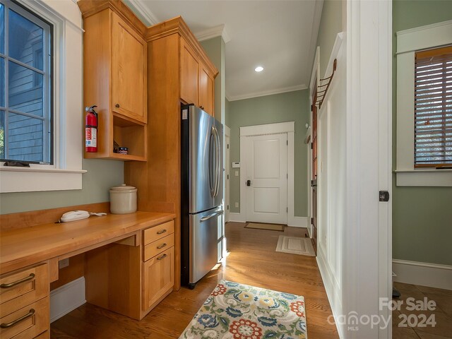 kitchen featuring built in desk, stainless steel fridge, ornamental molding, and light wood-type flooring