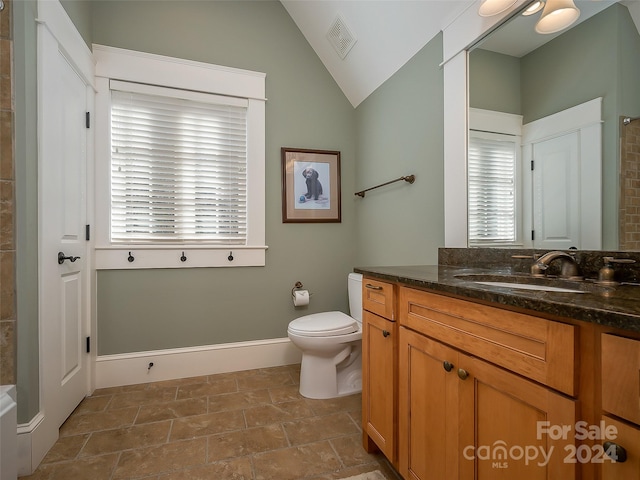 bathroom featuring toilet, plenty of natural light, vanity with extensive cabinet space, lofted ceiling, and tile flooring