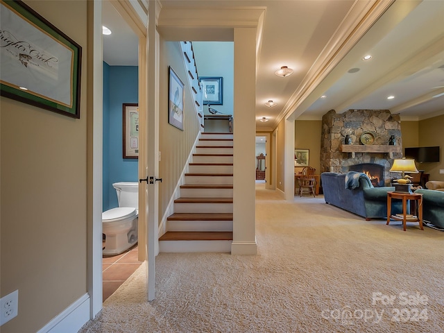 stairway with a fireplace, ornamental molding, and light colored carpet