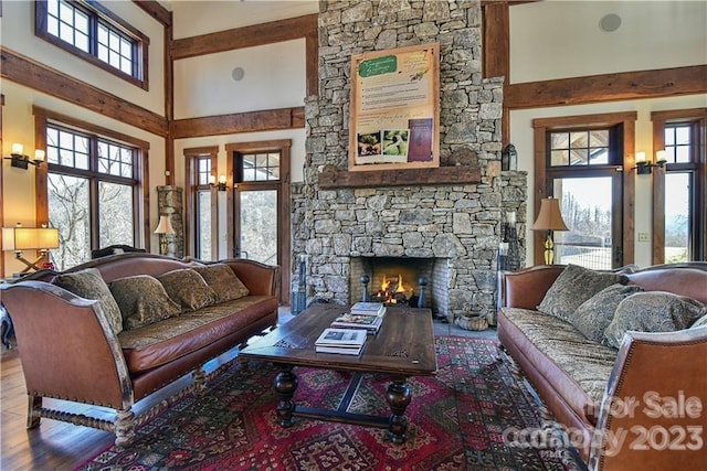 living room featuring a towering ceiling, a stone fireplace, and hardwood / wood-style flooring