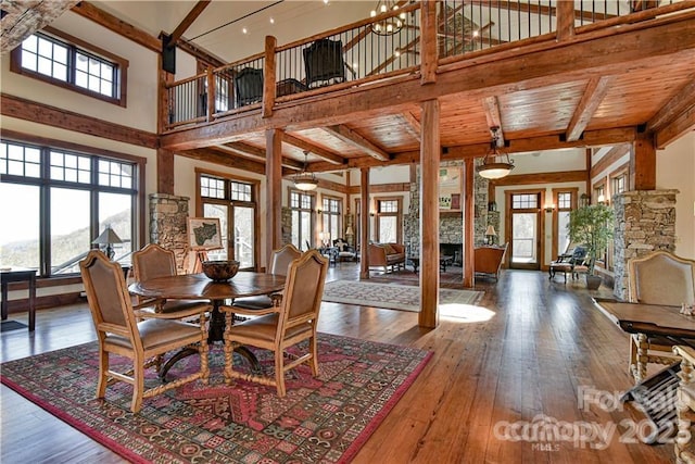 dining area featuring dark hardwood / wood-style flooring, a fireplace, beamed ceiling, and a towering ceiling