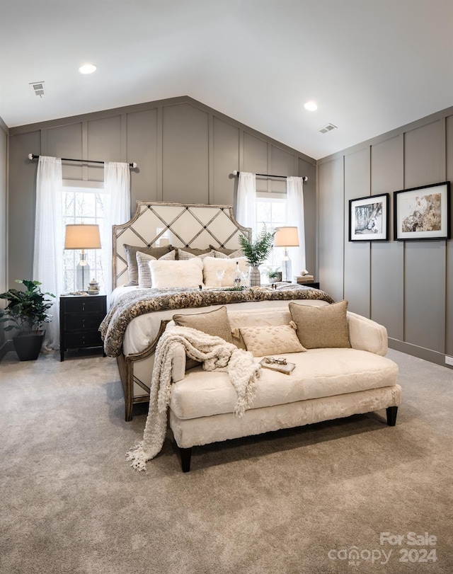 bedroom with lofted ceiling, a decorative wall, visible vents, and light carpet