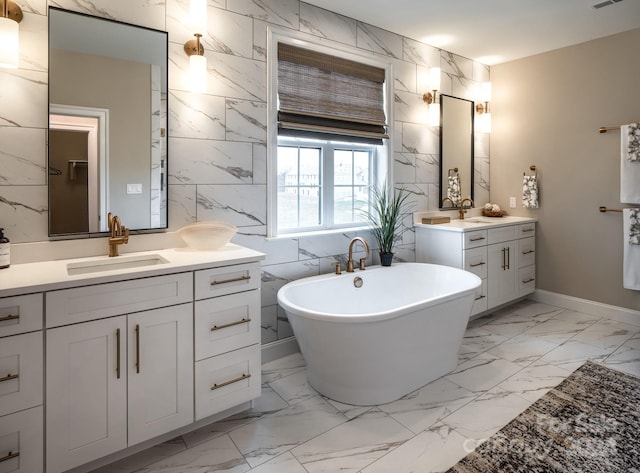 bathroom featuring marble finish floor, a freestanding tub, two vanities, and a sink