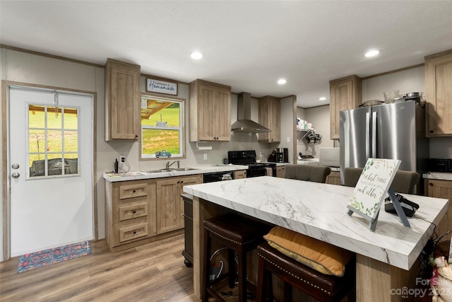 kitchen with a kitchen bar, light hardwood / wood-style flooring, black appliances, wall chimney range hood, and sink