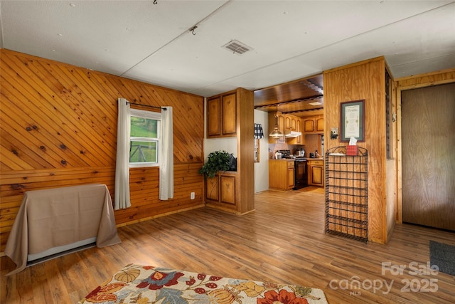 interior space featuring wooden walls, black electric range oven, and light wood-type flooring