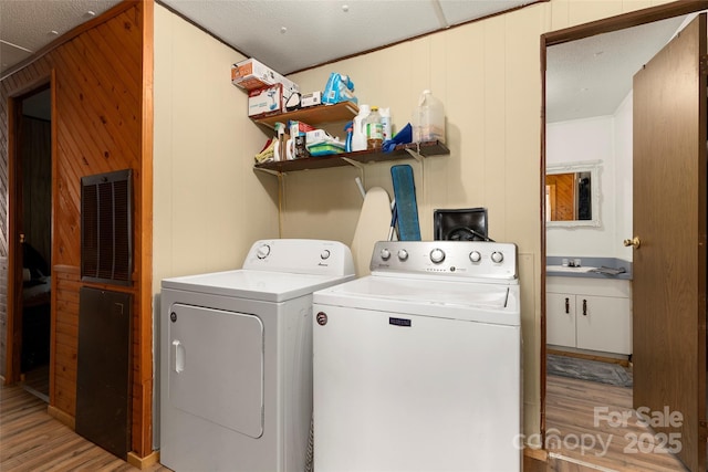 laundry area featuring wooden walls, sink, washer and dryer, and light wood-type flooring