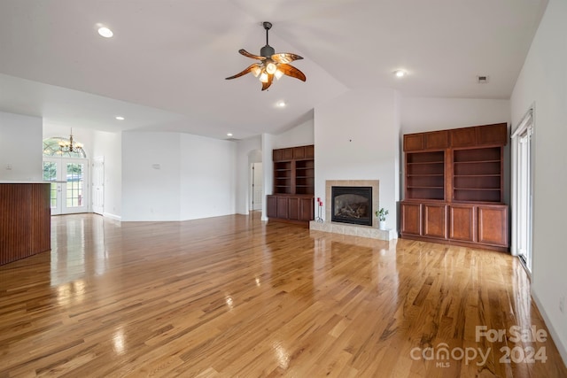 unfurnished living room with light wood-type flooring, a fireplace, high vaulted ceiling, and ceiling fan with notable chandelier