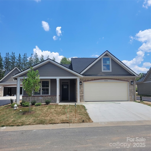 view of front of property with driveway, stone siding, covered porch, a front yard, and a garage