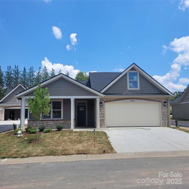 view of front of property with driveway, stone siding, covered porch, a front yard, and a garage