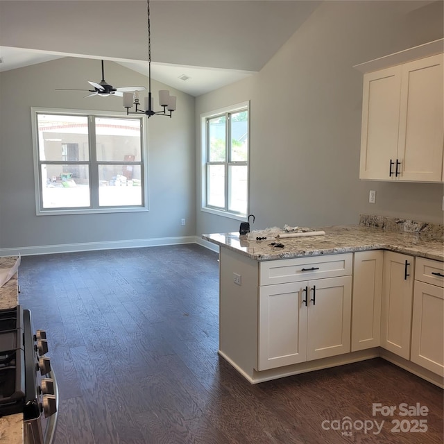 kitchen featuring light stone counters, a peninsula, lofted ceiling, dark wood-style flooring, and white cabinetry