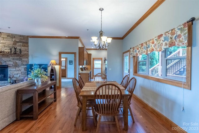 dining room with crown molding, a notable chandelier, a stone fireplace, and hardwood / wood-style flooring