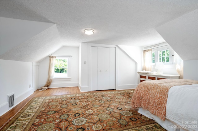 bedroom with a closet, a textured ceiling, light wood-type flooring, and vaulted ceiling