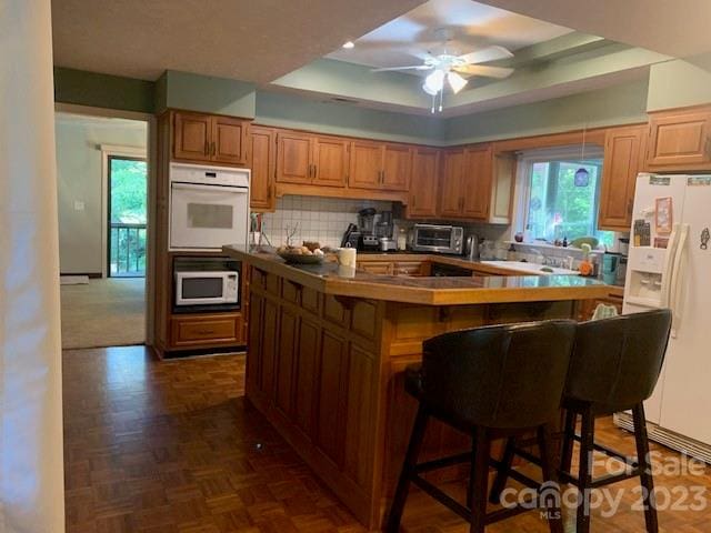 kitchen with dark parquet floors, white appliances, ceiling fan, a breakfast bar, and tasteful backsplash