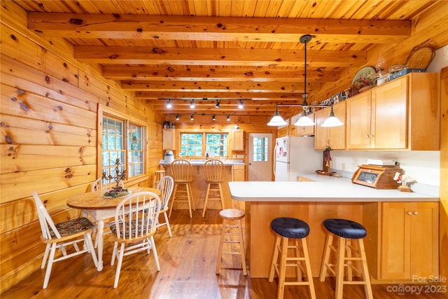 kitchen with kitchen peninsula, pendant lighting, white fridge, light hardwood / wood-style flooring, and beam ceiling