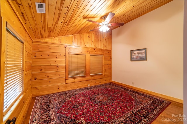 empty room with ceiling fan, wood ceiling, wood-type flooring, wood walls, and vaulted ceiling