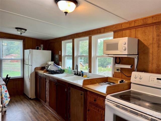 kitchen with dark hardwood / wood-style floors, white appliances, wooden walls, sink, and vaulted ceiling