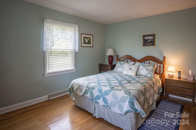 bedroom featuring a baseboard heating unit, ornamental molding, and wood-type flooring