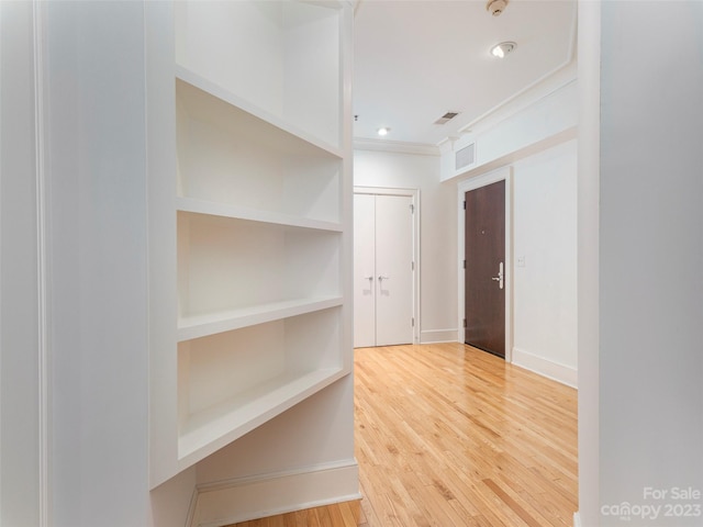 hallway featuring ornamental molding, built in shelves, and light hardwood / wood-style flooring