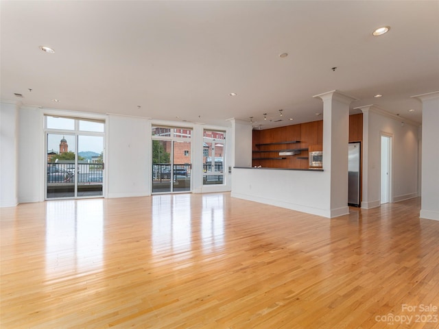 unfurnished living room featuring crown molding, decorative columns, and light hardwood / wood-style flooring