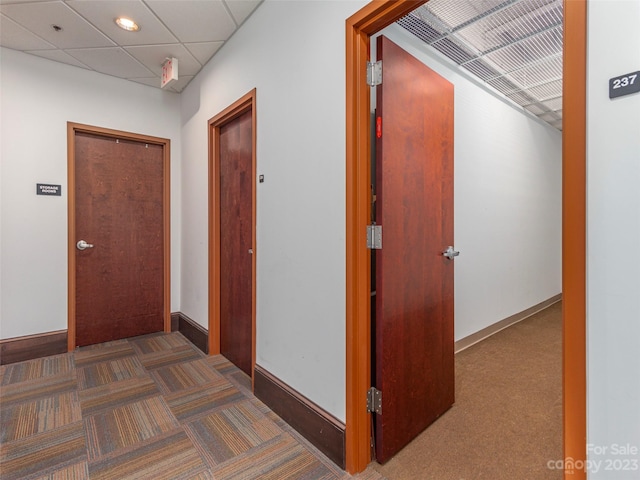 corridor featuring dark carpet and a drop ceiling