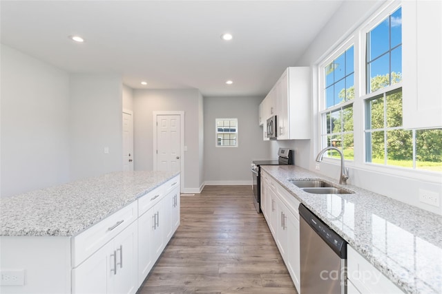 kitchen with light wood-type flooring, white cabinets, appliances with stainless steel finishes, light stone counters, and sink