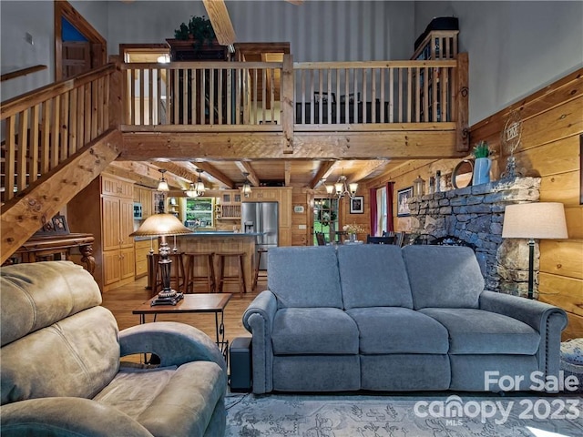 living room with wooden walls, an inviting chandelier, a fireplace, beam ceiling, and light wood-type flooring