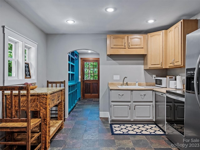 kitchen with appliances with stainless steel finishes, gray cabinetry, dark tile flooring, sink, and light brown cabinets