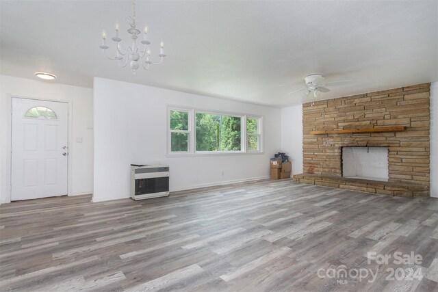 unfurnished living room with heating unit, a stone fireplace, light hardwood / wood-style flooring, and ceiling fan with notable chandelier