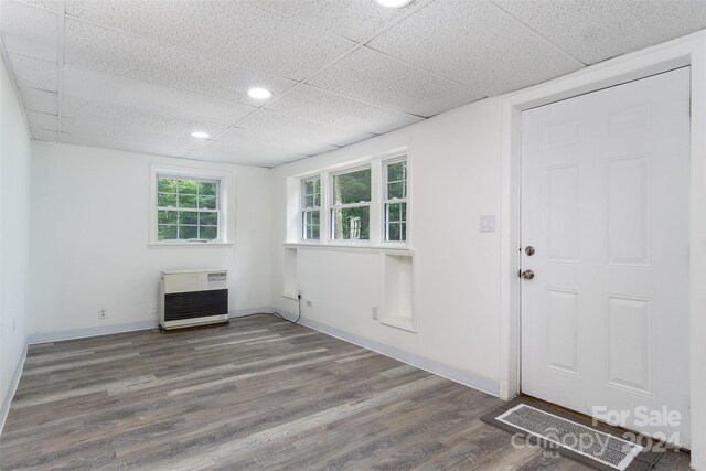 interior space with dark wood-type flooring, heating unit, and a drop ceiling