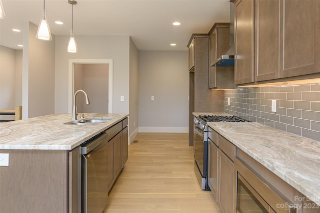 kitchen featuring appliances with stainless steel finishes, decorative light fixtures, an island with sink, sink, and light stone countertops