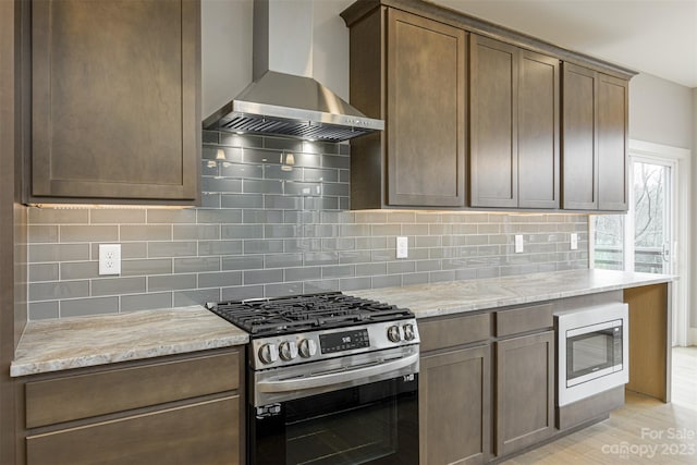 kitchen with stainless steel appliances, light stone countertops, decorative backsplash, and wall chimney range hood