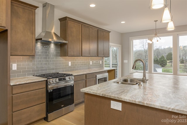 kitchen featuring pendant lighting, sink, light stone counters, gas range, and wall chimney exhaust hood