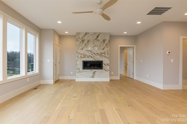 unfurnished living room featuring plenty of natural light, light hardwood / wood-style floors, a premium fireplace, and ceiling fan