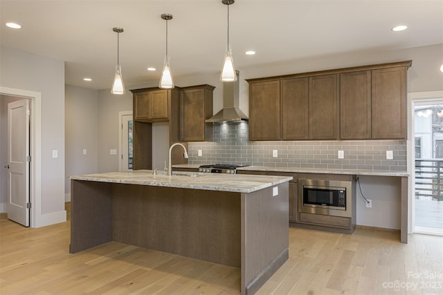 kitchen featuring sink, light wood-type flooring, stainless steel microwave, decorative backsplash, and wall chimney range hood