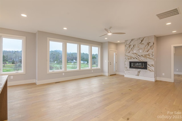 unfurnished living room featuring light hardwood / wood-style flooring, ceiling fan, a high end fireplace, and a healthy amount of sunlight