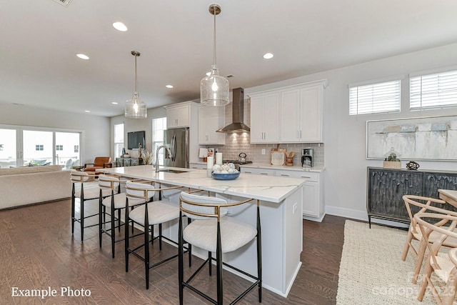 kitchen featuring an island with sink, white cabinetry, pendant lighting, and wall chimney range hood