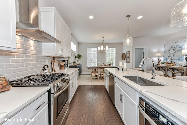 kitchen with decorative light fixtures, an inviting chandelier, appliances with stainless steel finishes, white cabinets, and wall chimney exhaust hood