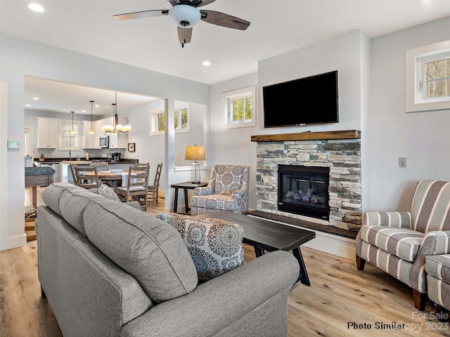 living room featuring a fireplace, ceiling fan with notable chandelier, and light hardwood / wood-style flooring