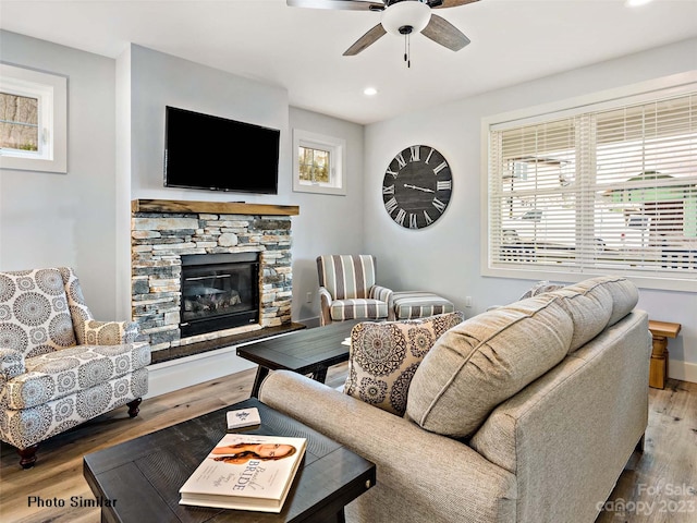 living room with a stone fireplace, ceiling fan, and wood-type flooring