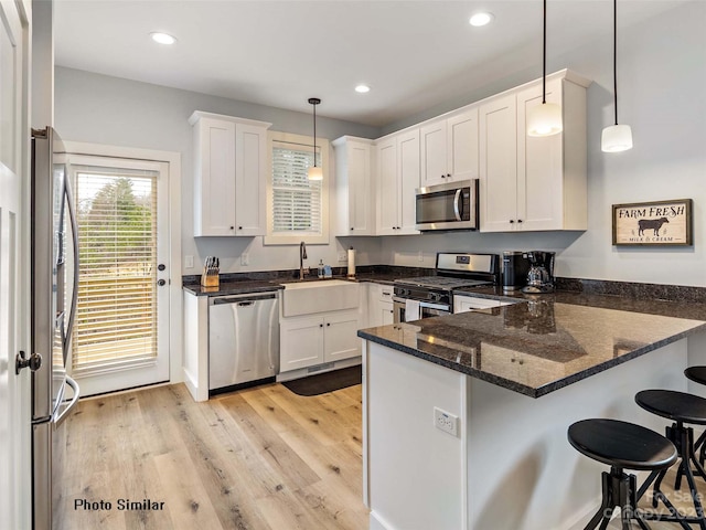 kitchen with stainless steel appliances, decorative light fixtures, sink, kitchen peninsula, and light hardwood / wood-style flooring