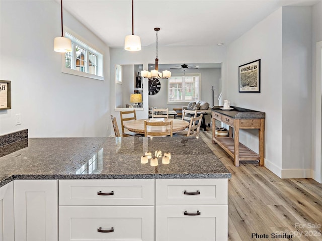 kitchen featuring white cabinets, pendant lighting, dark stone counters, and light wood-type flooring