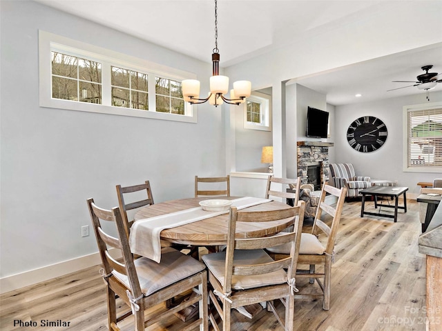 dining room with light hardwood / wood-style floors, ceiling fan with notable chandelier, and a fireplace