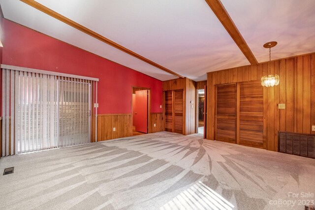 unfurnished bedroom featuring light carpet, an inviting chandelier, wooden walls, and vaulted ceiling with beams