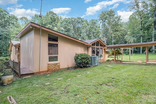 rear view of property with a carport, central AC, and a lawn