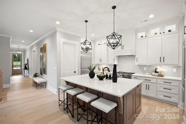 kitchen with white cabinets, an island with sink, ornamental molding, and light hardwood / wood-style floors