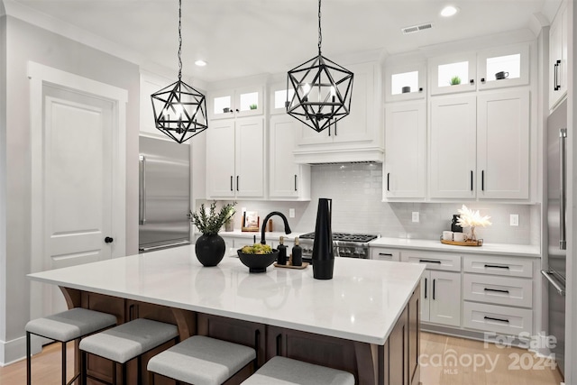 kitchen featuring decorative light fixtures, an island with sink, stainless steel appliances, and white cabinetry