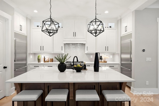 kitchen featuring decorative light fixtures, an island with sink, stainless steel built in fridge, and a kitchen bar