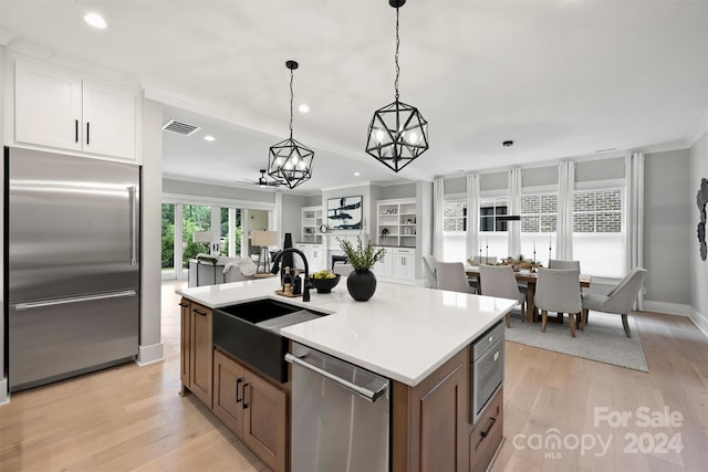 kitchen featuring a center island with sink, stainless steel appliances, hanging light fixtures, sink, and white cabinetry