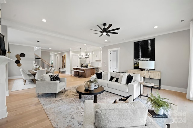 living room with ceiling fan with notable chandelier, ornamental molding, and light hardwood / wood-style floors