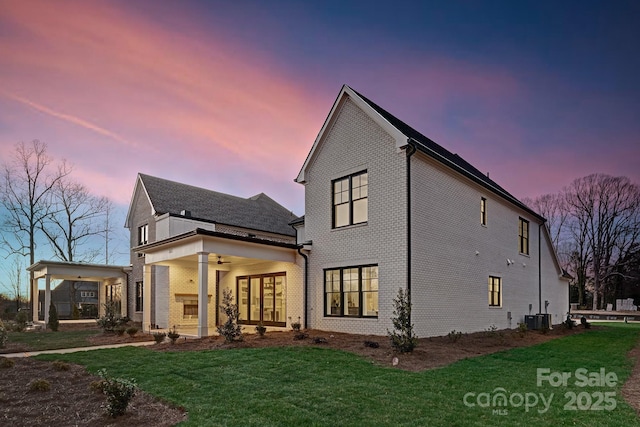 back of property featuring a lawn, a ceiling fan, cooling unit, and brick siding